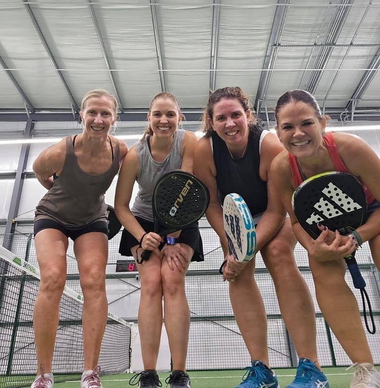 Cuatro mujeres sonriendo en cancha de pádel con raquetas
